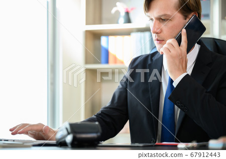 Young business man sitting at his desk working in office room Young business man sitting at his desk working in office room 67912443