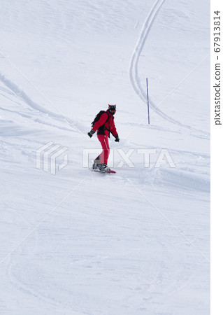 Snowboarder in red descends on snowy ski slope 67913814