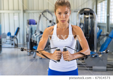 Fitness woman working out in gym with cable tower. Fit Asian girl training toned arms and body Fitness woman working out in gym with cable tower. Fit Asian girl training toned arms and body 67914573
