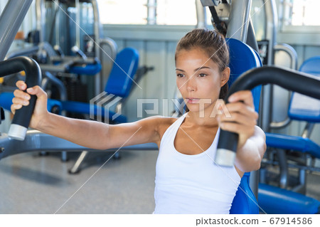 Gym workout Asian woman focused and motivated training on pec deck fly machine. Fitness workout 67914586