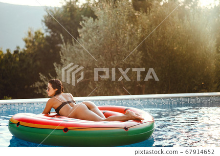 Sexy woman relax in pool laying on inflatable pool toy watermelon on vacations 67914652