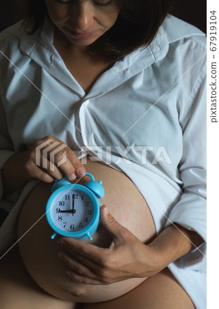 High angle of crop pregnant female holding alarm clock on belly while waiting for baby. 67919104