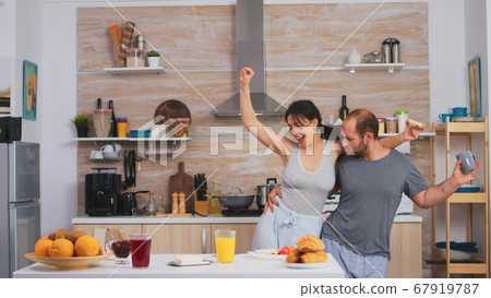 Carefree couple dancing and singing in kitchen Carefree couple dancing and singing in kitchen 67919787