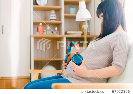 Pregnant woman pregnant with headphones on her stomach Pregnant woman pregnant with headphones on her stomach 67922596