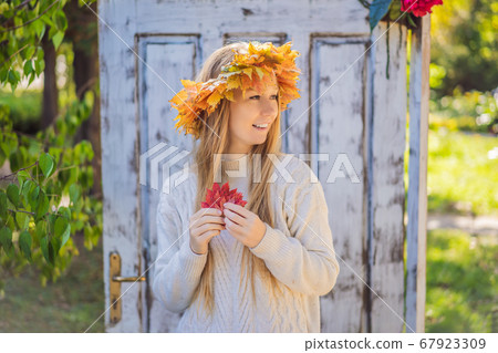 Outdoors lifestyle close up portrait of charming blonde young woman wearing a wreath of autumn leaves. Wearing stylish knitted pullover. Wreath of maple leaves 67923309