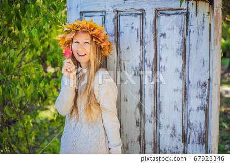 Outdoors lifestyle close up portrait of charming blonde young woman wearing a wreath of autumn leaves. Wearing stylish knitted pullover. Wreath of maple leaves 67923346