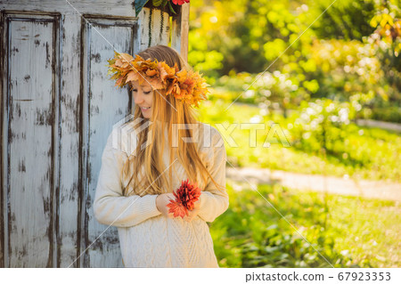 Outdoors lifestyle close up portrait of charming blonde young woman wearing a wreath of autumn leaves. Wearing stylish knitted pullover. Wreath of maple leaves Outdoors lifestyle close up portrait of charming blonde young woman wearing a wreath of autumn leaves. Wearing stylish knitted pullover. Wreath of maple leaves 67923353