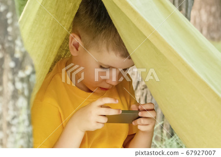 Child reading e-book. Online education. E-learning background. Little boy with cell phone playing video game. Alternative education. Quarantine and studying. E-courses background. Prepare to school Child reading e-book. Online education. E-learning background. Little boy with cell phone playing video game. Alternative education. Quarantine and studying. E-courses background. Prepare to school 67927007