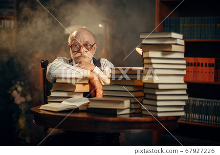 Elderly writer sitting at the table with books Elderly writer sitting at the table with books 67927226