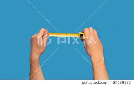 Handyman holding tape measure on blue background, closeup view Handyman holding tape measure on blue background, closeup view 67929183