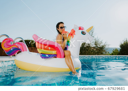 woman lay on inflatable pool toy unicorn in swimming pool and eat watermelon woman lay on inflatable pool toy unicorn in swimming pool and eat watermelon 67929681