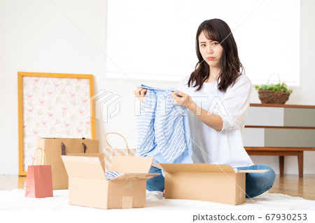 A young woman who takes out clothes bought at an online shop from cardboard and decides on items 67930253
