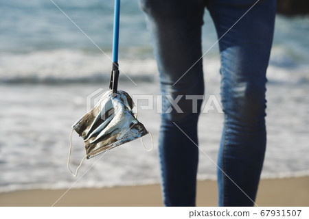 collecting a used surgical mask on the beach 67931507