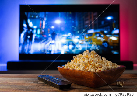 A wooden bowl of popcorn and remote control. A wooden bowl of popcorn and remote control. 67933956