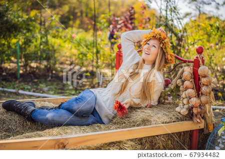 Outdoors lifestyle close up portrait of charming blonde young woman wearing a wreath of autumn leaves on a haystack. Wearing stylish knitted pullover. Wreath of maple leaves Outdoors lifestyle close up portrait of charming blonde young woman wearing a wreath of autumn leaves on a haystack. Wearing stylish knitted pullover. Wreath of maple leaves 67934482