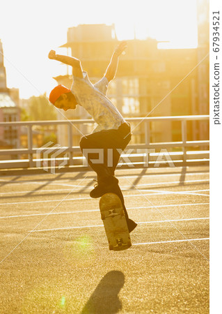 Skateboarder doing a trick at the city's street in summer's sunshine Skateboarder doing a trick at the city's street in summer's sunshine 67934521