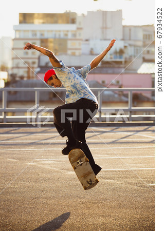 Skateboarder doing a trick at the city's street in summer's sunshine Skateboarder doing a trick at the city's street in summer's sunshine 67934522