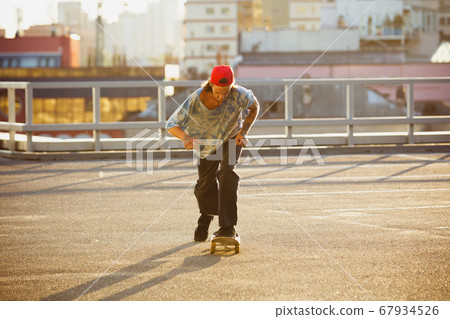 Skateboarder doing a trick at the city's street in summer's sunshine Skateboarder doing a trick at the city's street in summer's sunshine 67934526