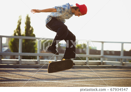 Skateboarder doing a trick at the city's street in summer's sunshine Skateboarder doing a trick at the city's street in summer's sunshine 67934547