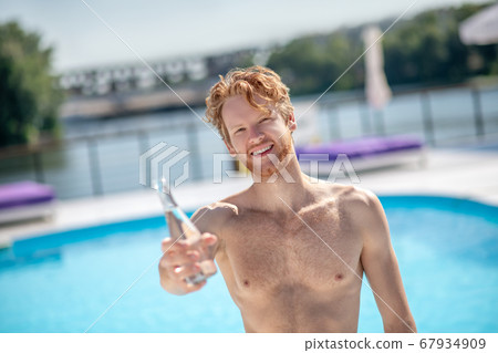 Red-haired man holding out bottle of drinking water. 67934909