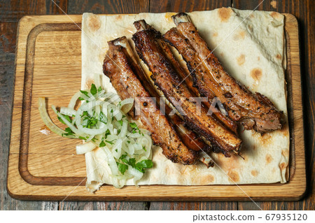 Spicy hot grilled spare ribs from a summer BBQ served with a hot chili pepper and fresh tomatoes on an old vintage wooden cutting board. 67935120