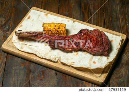 Freshly grilled Tomahawk steaks on wooden cutting board with corn Freshly grilled Tomahawk steaks on wooden cutting board with corn 67935159