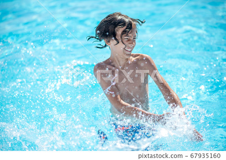 Energetic boy standing in water making splashes Energetic boy standing in water making splashes 67935160