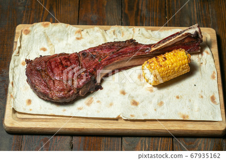 Freshly grilled Tomahawk steaks on wooden cutting board with corn Freshly grilled Tomahawk steaks on wooden cutting board with corn 67935162