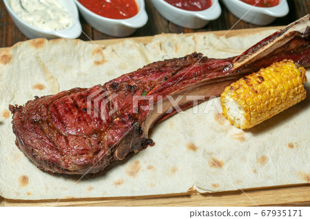 Freshly grilled Tomahawk steaks on wooden cutting board with corn Freshly grilled Tomahawk steaks on wooden cutting board with corn 67935171