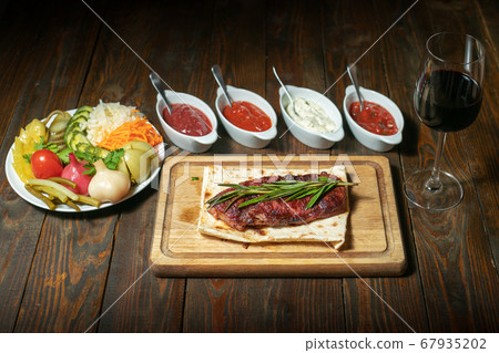 Fried steak with vegetables and sauces on wooden board 67935202