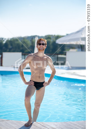 Muscular man in swimming suit standing near pool 67935339