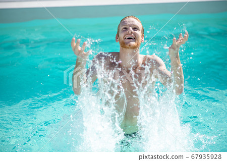 Young cheerful man in pool water splashing with water Young cheerful man in pool water splashing with water 67935928