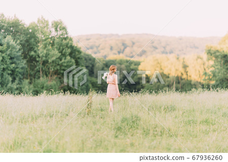 Beautiful young Caucasian blond woman in light dress holding bouquet of white peonies, walking in summer field or garden in sunset. Woman with flowers outdoors 67936260