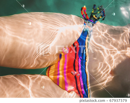 Woman in bright swimsuit with colorful stripes swims in sea. Top view on body through water. Woman in bright swimsuit with colorful stripes swims in sea. Top view on body through water. 67937379