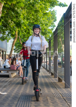 Trendy fashinable teenager girls riding public rental electric scooters in urban city environment. New eco-friendly modern public city transport in Ljubljana, Slovenia 67937641