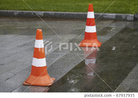 Side view of two bright orange-white warning cones Side view of two bright orange-white warning cones 67937935