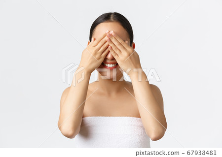 Beauty, cosmetology and spa salon concept. Close-up of silly happy, pretty asian girl in bath towel smiling upbeat as waiting with anticipation to open eyes, close eyes with hands, white background 67938481