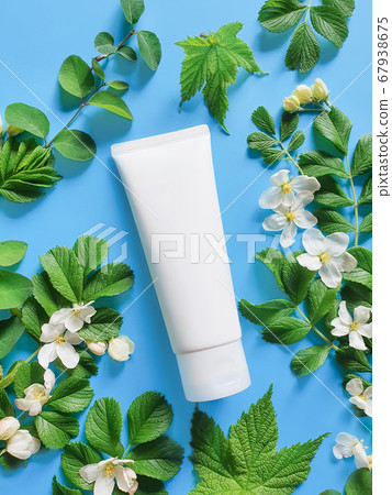 Cosmetics SPA branding mock-up with fresh green leaves and white flowers on a deep blue background. White plastic tube for branding, flower flat lay. Vertical photo. 67938675