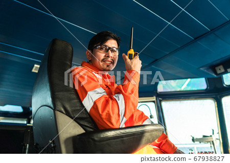 Filipino deck Officer on bridge of vessel or ship. He is speaking on GMDSS VHF radio 67938827