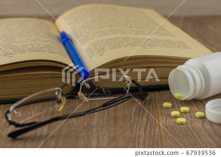 sleep deprivation at work: a box of caffeine pills, glasses, open book, blue pen - a view from above, close 67939536