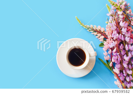 Cup of black coffee or hot chocolate and pink lupine flowers on a blue background. Aroma and good morning concept. Top view, flat lay lifestyle, copy space. Cup of black coffee or hot chocolate and pink lupine flowers on a blue background. Aroma and good morning concept. Top view, flat lay lifestyle, copy space. 67939582
