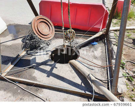 An open sewer manhole and a red guardrail. Repair work. 67939661