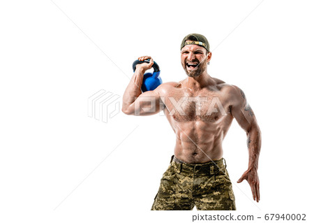Muscular athlete bodybuilder man in camouflage pants with a naked torso workout with kettlebell on a white background. Muscular athlete bodybuilder man in camouflage pants with a naked torso workout with kettlebell on a white background. 67940002