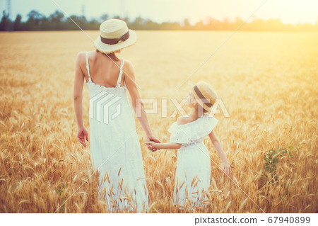 young mother and her daughter in white dress and straw hat at the wheat field on a sunny day young mother and her daughter in white dress and straw hat at the wheat field on a sunny day 67940899