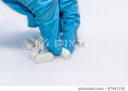Hand in blue glove takes white long pills on white Hand in blue glove takes white long pills on white 67941150