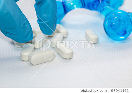 Hand in blue glove takes white long pills on white Hand in blue glove takes white long pills on white 67941151