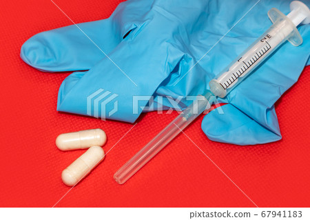 White 2 ml syringe macro on red, blue glove, pills White 2 ml syringe macro on red, blue glove, pills 67941183