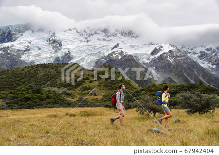 New Zealand travel hikers hiking on snow capped mountains landscape background. Couple trampers walking on Hooker Valley Track, popular tourist destination for summer vacation 67942404