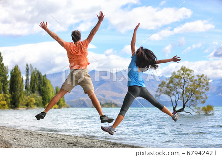 New Zealand tourists couple jumping of happiness at Wanaka Lone . Happy young people doing funny jump of joy sightseeing traveling in summer adventure destination. Woman and man 67942421