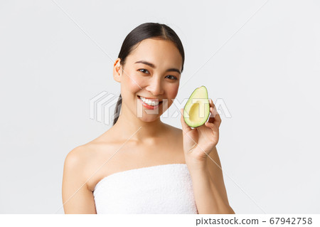 Beauty, personal care, spa and skincare concept. Close-up of beautiful asian female in bath towel showing avocado and smiling, recommend face mask or facial hydrating and nourishing cream Beauty, personal care, spa and skincare concept. Close-up of beautiful asian female in bath towel showing avocado and smiling, recommend face mask or facial hydrating and nourishing cream 67942758